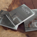 Photo of the ultimate elopement guide and destination wedding books randomly placed on table. Book is ELOPE by Sherry Martin Peters and the cover is of a bride and groom walking on a ledge in Isle of Skye Scotland, adventure eloping